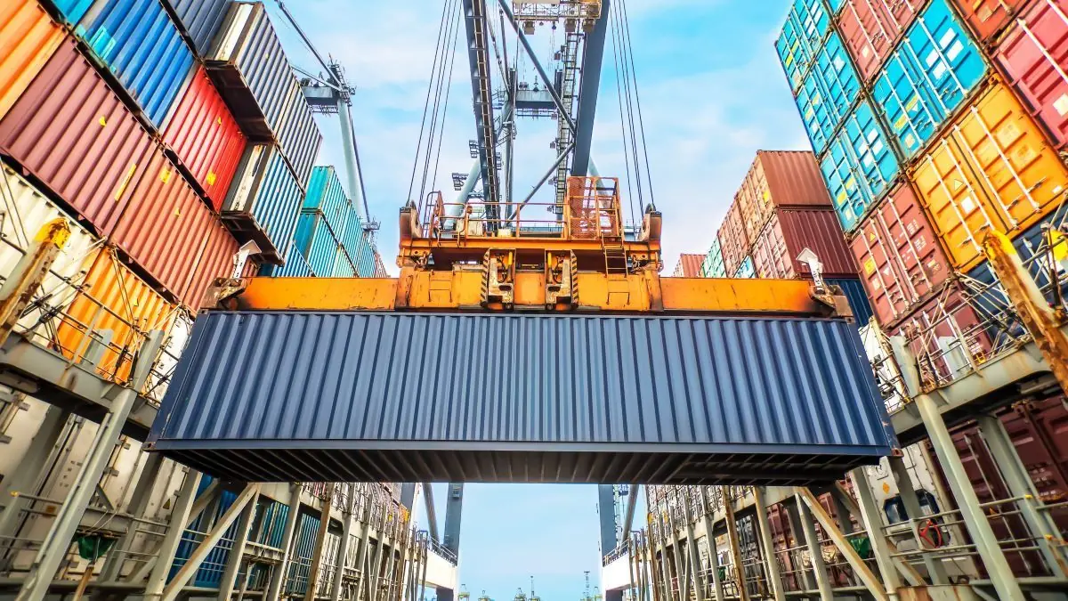 Crane lifting a shipping container between container stacks
